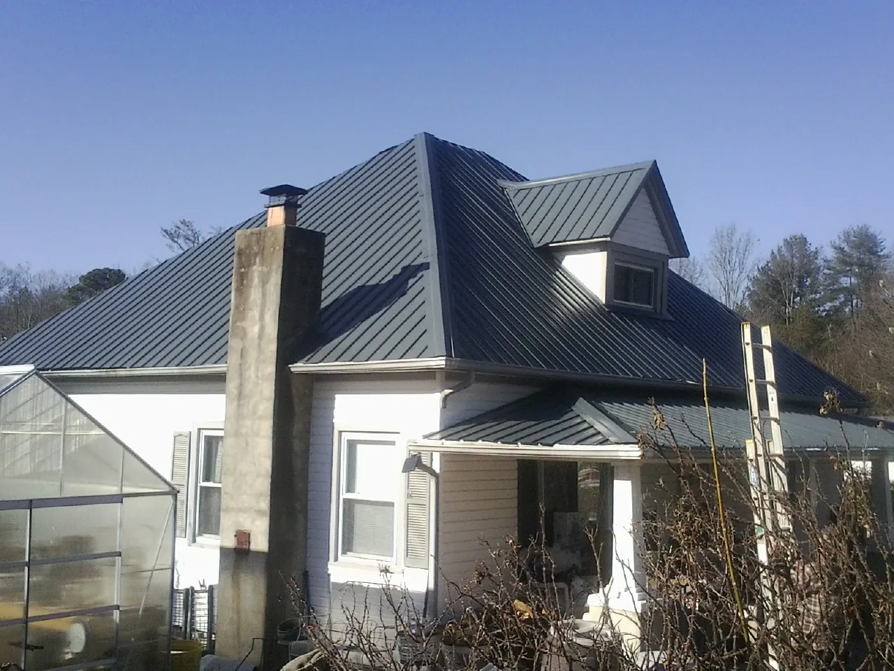 Dark blue standing seam metal roof on a white farmhouse with dormer — Slate & Tile Roof Repair by Roofing Brothers in South Dartmouth