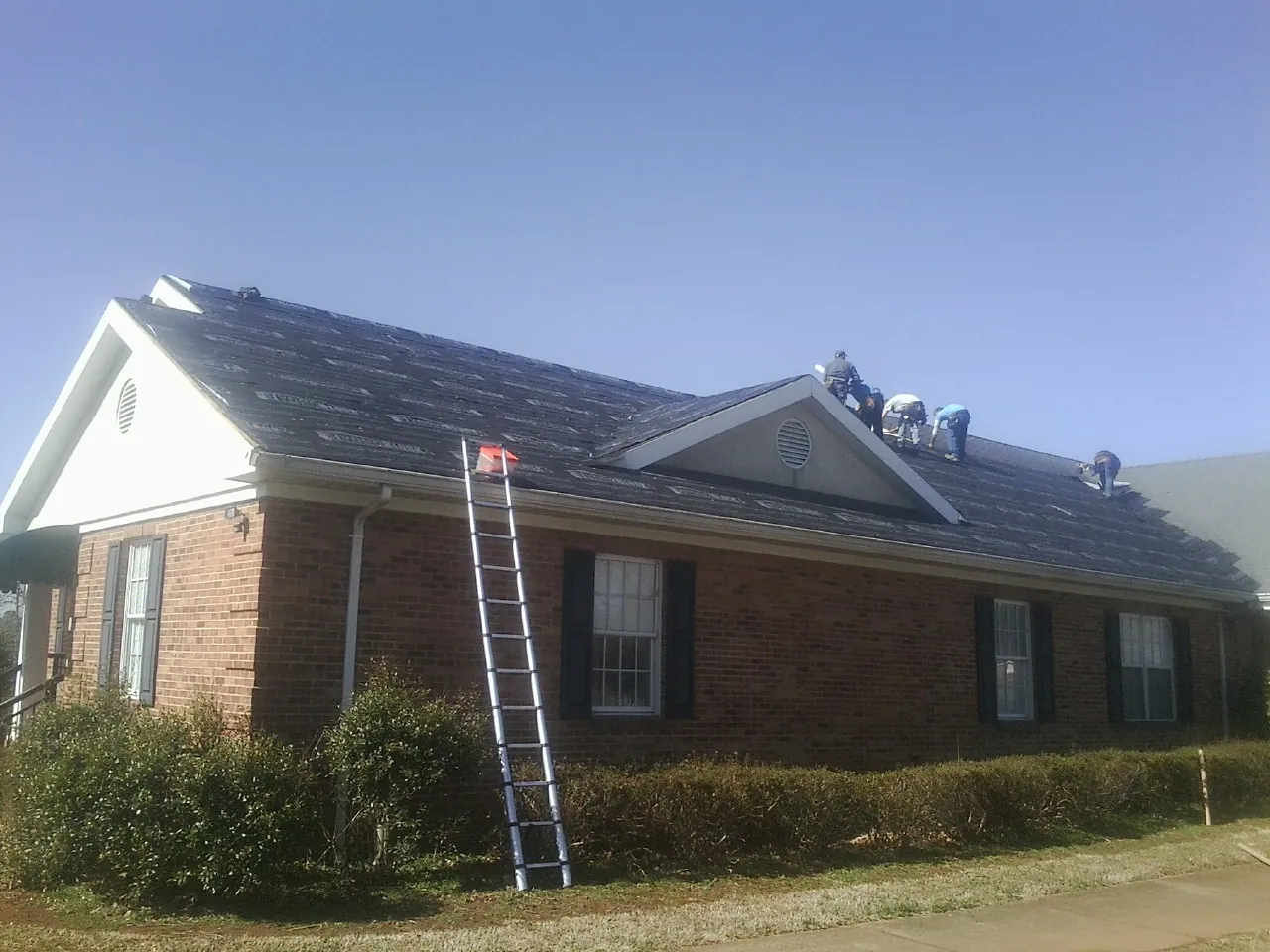 Crew tearing shingles off a brick ranch roof with a ladder set — Metal Roof Repair work by our crew in South Dartmouth