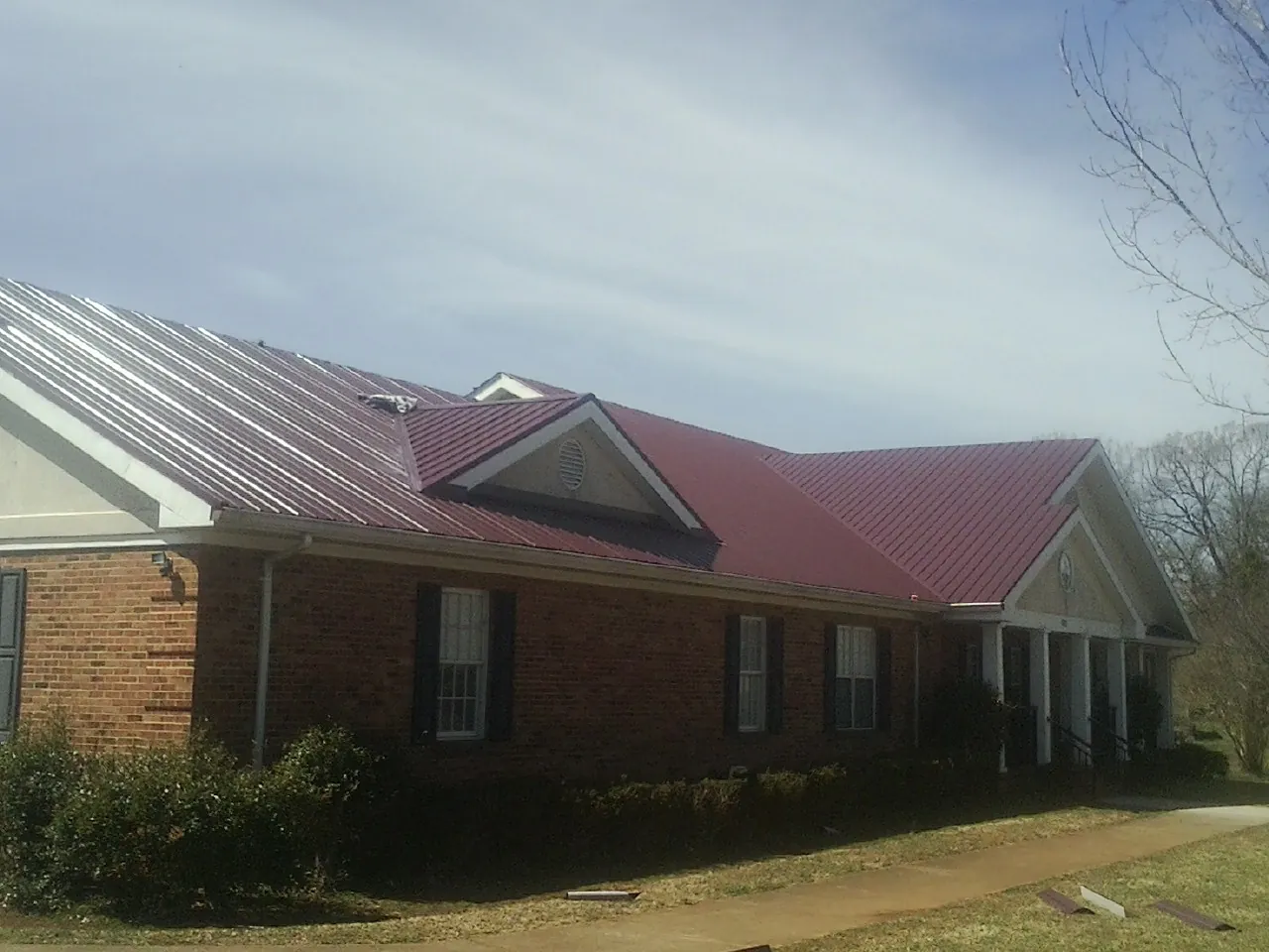 Red metal roof with gabled entries on a long brick building, from a Hail Damage Roof Repair job in South Dartmouth