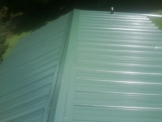 New green metal panels meeting at the ridge of a roof — Flat Roof Repair work by our crew in South Dartmouth