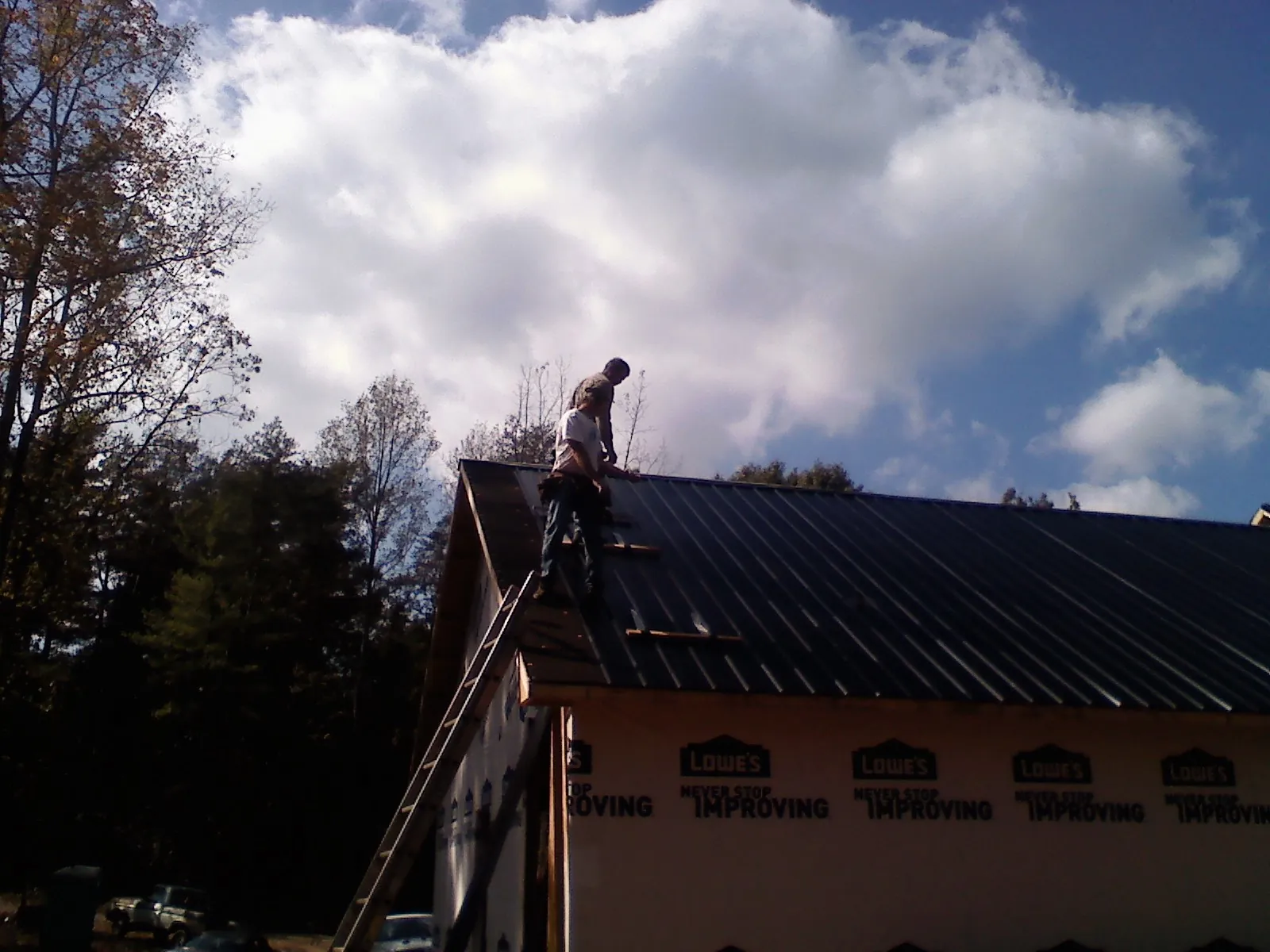 Roofer fastening dark metal panels high against a cloudy sky, from a Roof Inspection job in South Dartmouth