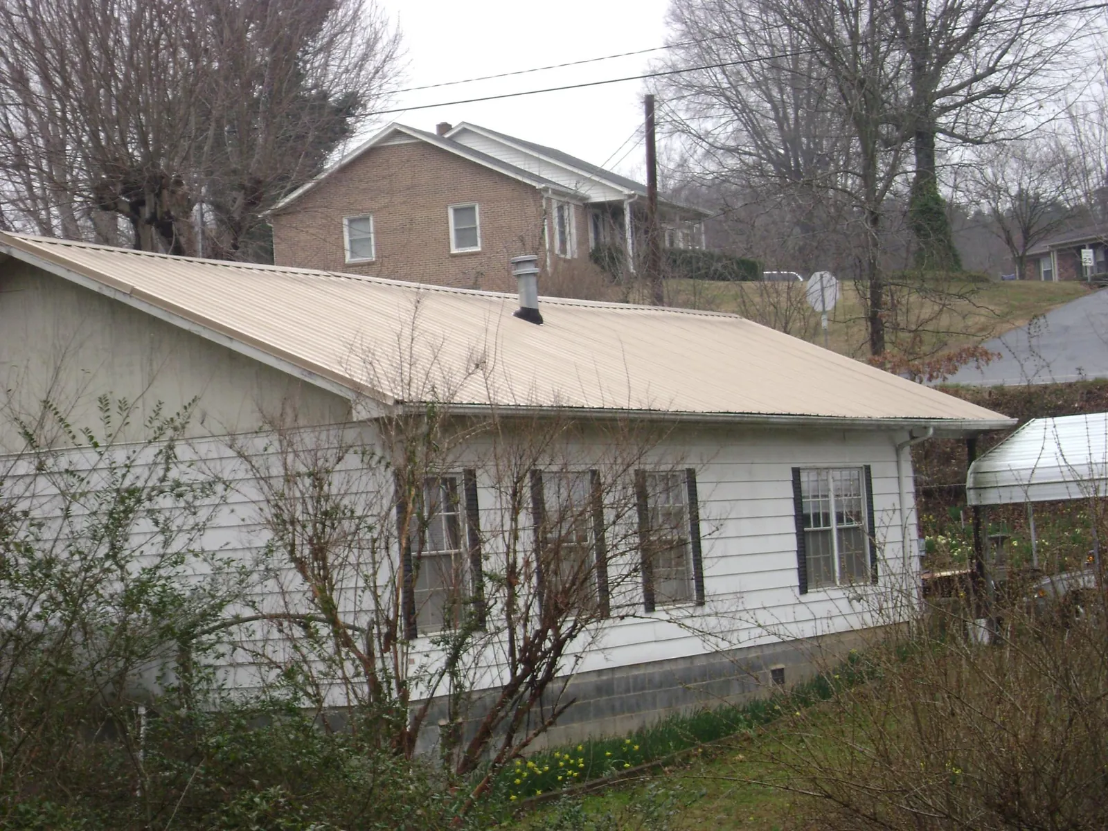 Tan metal roof on a white sided house set into a hillside — Commercial Roofing by Roofing Brothers in South Dartmouth
